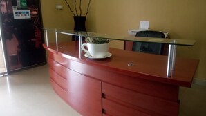 A reception desk with a glass top, a white cup with flowers, and a black chair.