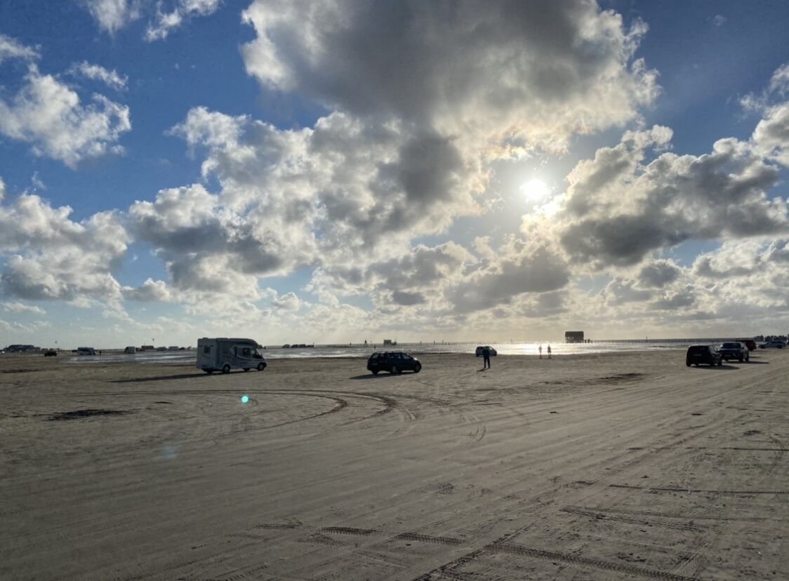 Une vaste étendue de sable, à ciel ouvert, où se trouvent quelques véhicules et quelques personnes, sous un ciel partiellement nuageux.