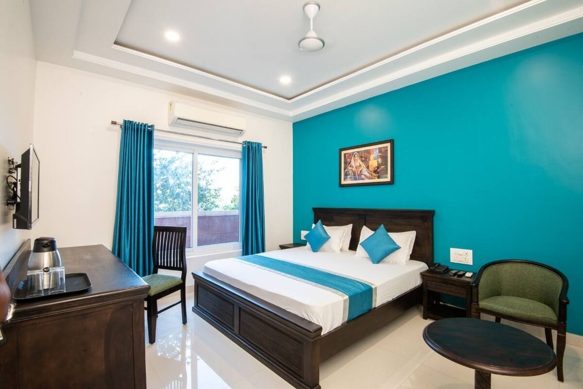 A hotel room with a bed, a desk with a coffee maker, a chair, and a nightstand with a phone.
