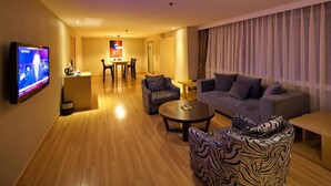 A modern living room with a flat-screen TV, a sofa, a patterned armchair, and a dining area with a table and chairs. - Mareka Origin Hotel (Chengdu)