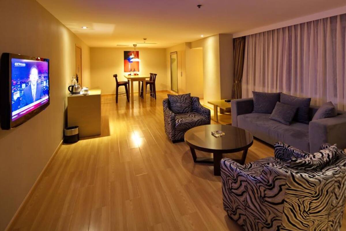 A modern living room with a flat-screen TV, a sofa, a patterned armchair, and a dining area with a table and chairs.