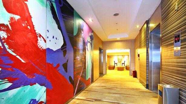 A hotel corridor with a colorful abstract mural on the left, a wooden floor, and a closed elevator on the right. - Mareka Origin Hotel (Chengdu)