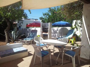 Eine Terrassengruppe im Freien mit rundem Tisch und Stühlen, umgeben von Sonnenschirmen und Blumentöpfen.