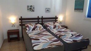 Ein Bett mit gemustertem Überwurf, zwei Nachttische, Wandleuchten und zwei gerahmte Bilder an der Wand.