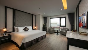 A hotel room with a large bed, a desk, a chair, a window with a view, and a balcony. - Sen Grand Hotel & Spa managed by Sen Group (Hanoi)