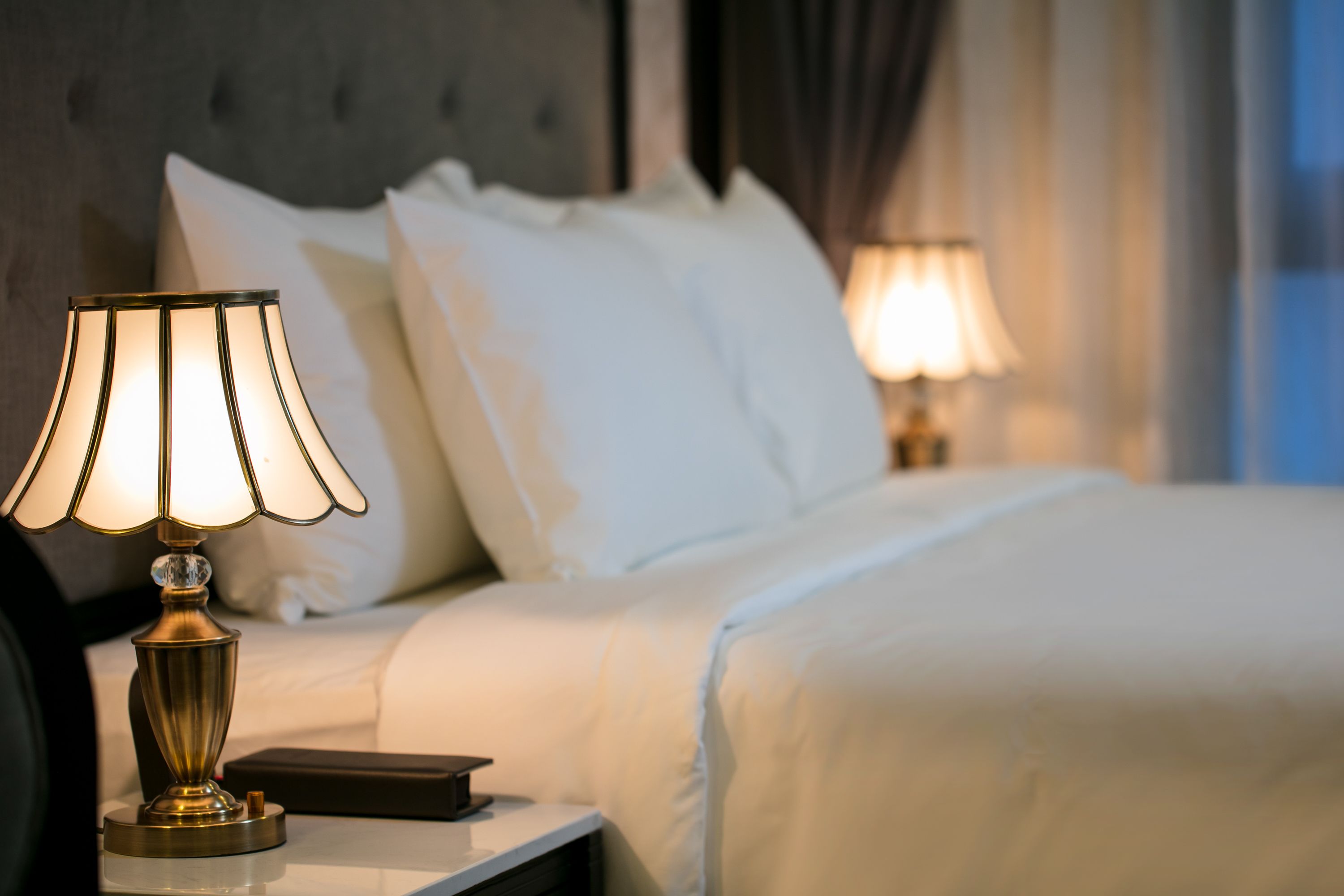 A neatly made bed with white linens, a bedside lamp, and a book on the nightstand.
