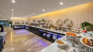 A modern hotel lobby with a marble reception desk, a buffet area with various food items, and a seating area with chairs. - Sen Grand Hotel & Spa managed by Sen Group (Hanoi)