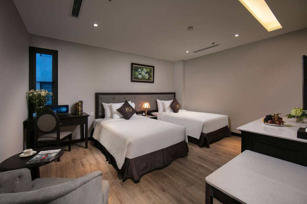 Een hotelkamer met twee bedden, een bureau, een stoel, een eettafel en een raam.