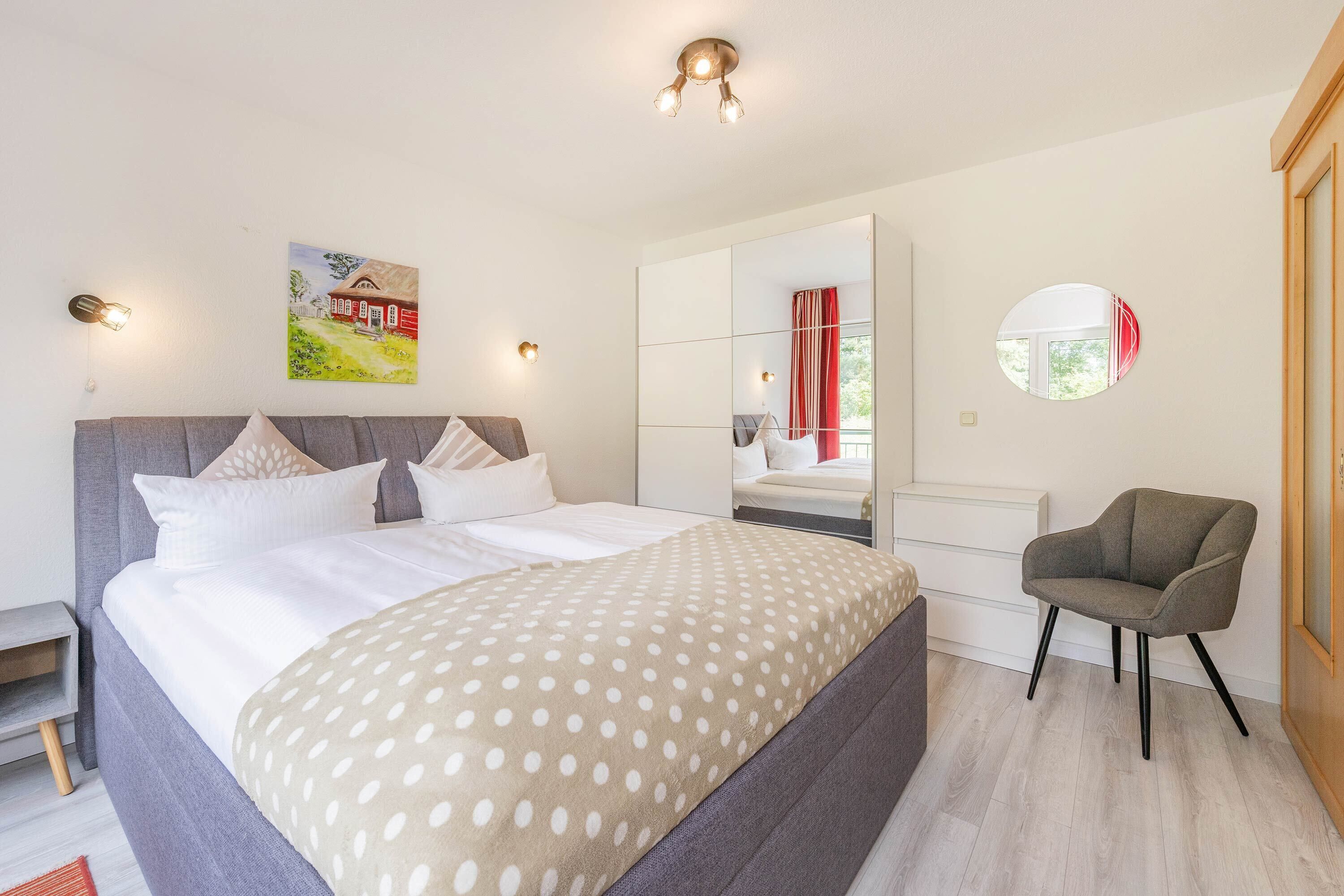 Een slaapkamer met een bed, een stoel, een kaptafel, een spiegel en een schilderij aan de muur.