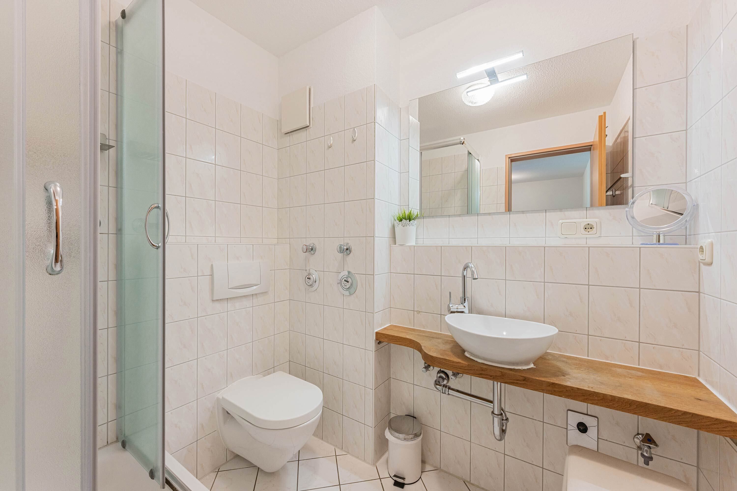 Ein modernes Badezimmer mit Duschkabine aus Glas, Toilette in Weiß, Holzwaschtisch und Spiegel.