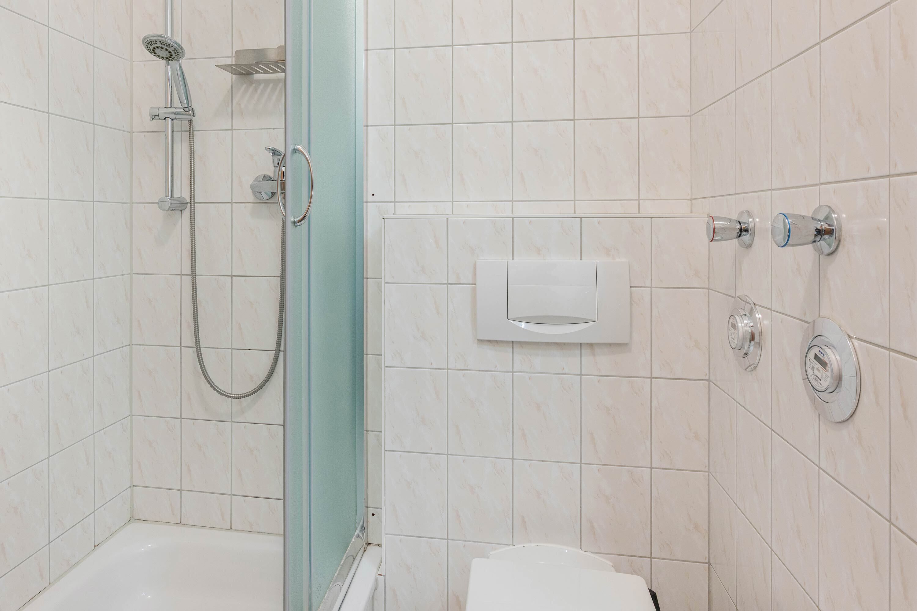 A bathroom with a shower, toilet, and a towel dispenser.