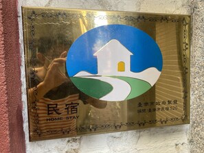 Un cartel enmarcado con un gráfico de una casa, texto en chino e inglés, y el reflejo de una persona.