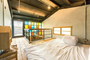 Un dormitorio con cama, una silla de madera, un ventanal con vistas y un separador de vidrio colorido.