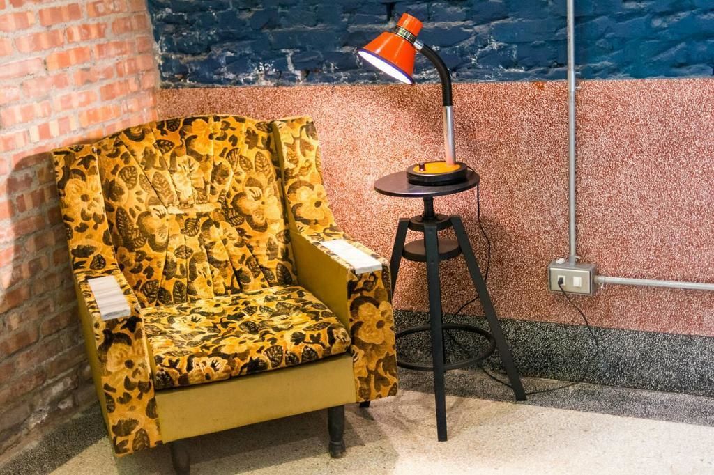 A yellow armchair with a leopard print pattern, a black floor lamp, and a brick wall.