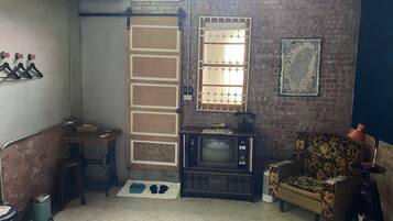 A compact living space with a brick wall, a vintage television, a patterned armchair, and a small table with a lamp.