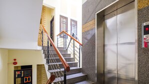 A staircase with a handrail, a wall-mounted elevator, and a door with a red emergency light. - Coop's Hotel & Apartments (Da Nang)