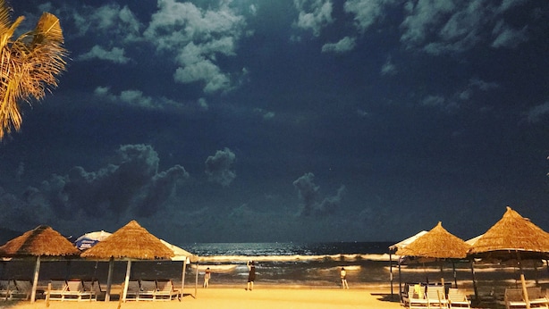A beach with thatched-roof huts and sun loungers. - Coop's Hotel & Apartments (Da Nang)
