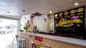 A hotel reception area with a marble counter, two wooden bar stools, a decorative wall with clocks and a neon sign, and a large window overlooking the street. - Coop's Hotel & Apartments (Da Nang)