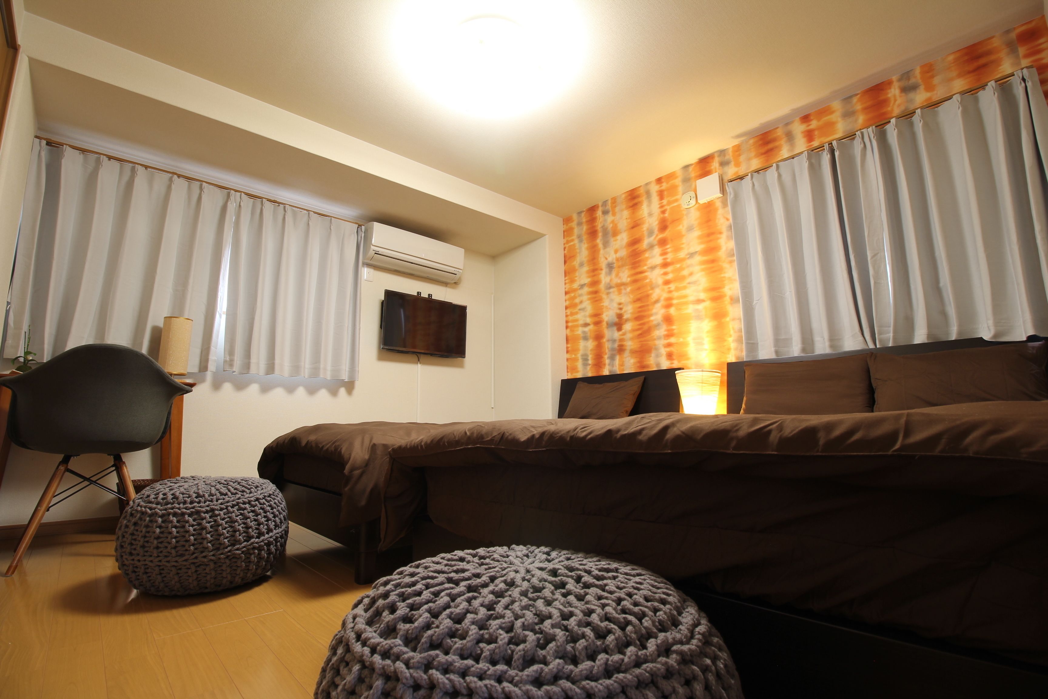 Ein Schlafzimmer mit einem Bett, zwei Poufs, einem Sessel und einem Fernseher an der Wand.