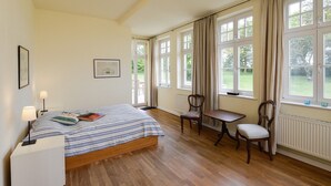 A bedroom with a bed, a chair, a table, and large windows.