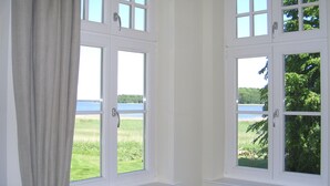 A room with two windows overlooking a grassy field and a body of water.