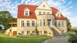 A large, two-story building with a red-tiled roof, multiple windows, and a central staircase leading to the upper floor.