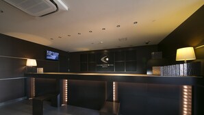 Un mostrador de recepción con una pantalla digital, un cartel del Hotel Centre One y un banco.