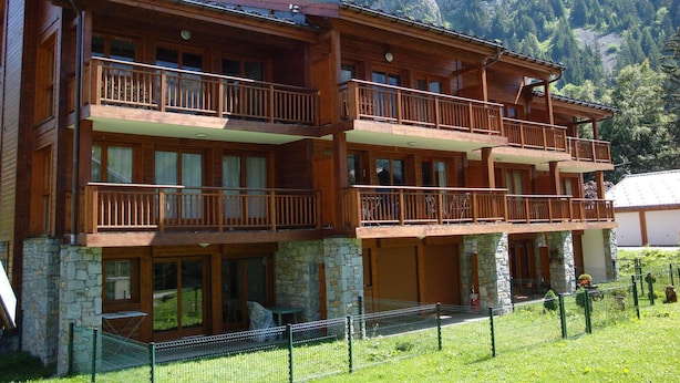 A multi-story wooden building with balconies, stone foundation, and a mountainous backdrop. - Cozy and bright apartment with garden, for 6 guests (Pralognan-la-Vanoise)
