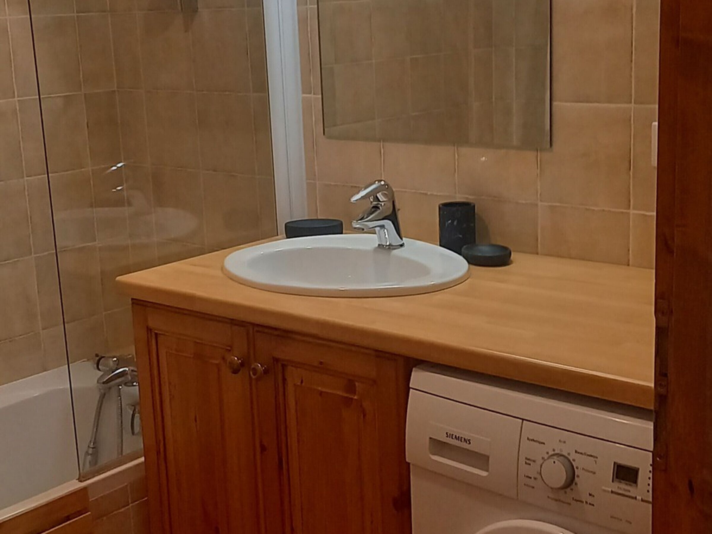 A bathroom with a white sink, wooden cabinets, a Siemens dishwasher, and a glass shower enclosure.