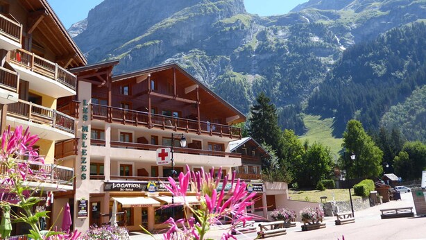 A hotel with multiple balconies, a ski rental sign, and a mountain backdrop. - Beautiful apartment in Pralognan center with parking (Pralognan-la-Vanoise)