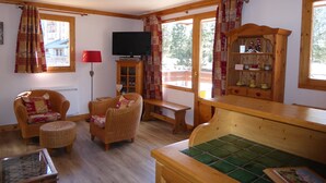 A cozy living room with wicker furniture, a television, and a wooden cabinet with decorative items. - Beautiful apartment in Pralognan center with parking (Pralognan-la-Vanoise)