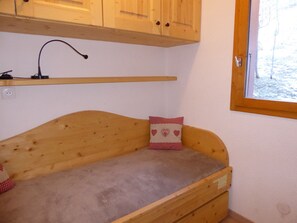 Eine Holzbank mit Kissen, ein kleines Regal darüber und ein Fenster mit Blick auf Bäume.