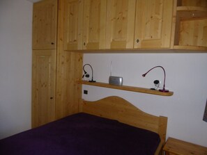 Une chambre avec des armoires en bois, un lit recouvert d’une courtepointe violette et deux lampes de chevet.