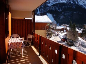 Ein Holzbalkon mit Tisch und Stühlen, mit Blick auf ein verschneites Dorf und Berge.