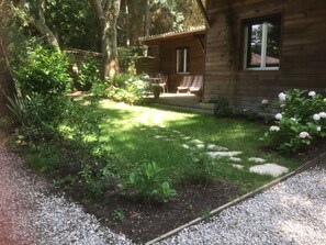 Una cabana de fusta amb un petit balcó i un jardí ple de plantes i flors diverses.