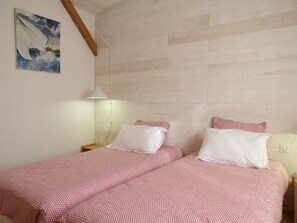 Un dormitori amb un capçal de llit de fusta, dos llits amb roba de llit vermella i blanca, una nitòria amb una làmpada i un quadre a la paret.