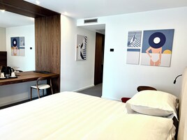 Et hotelværelse med en seng, et skrivebord med stol og billedkunst på væggene.