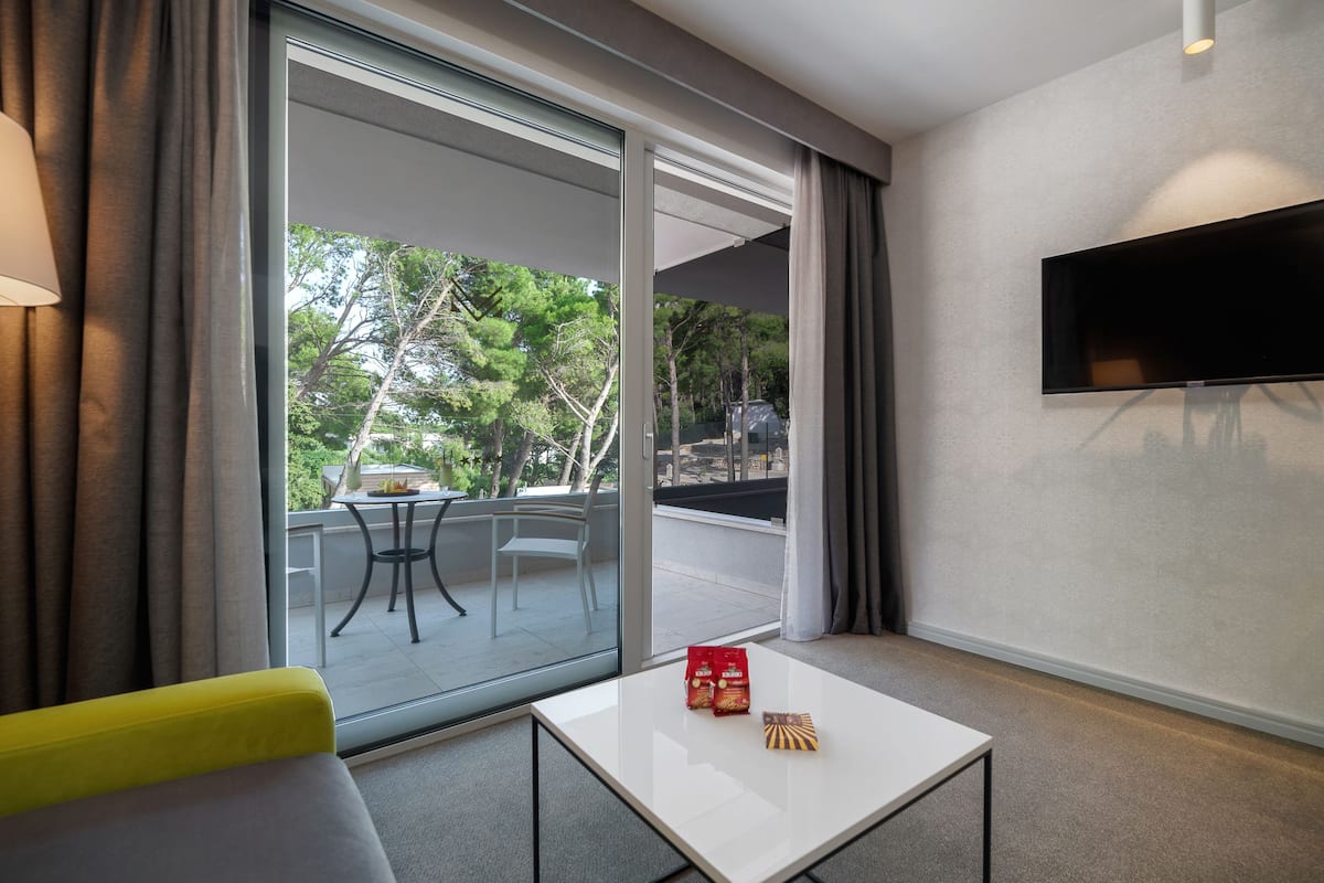 A hotel room with a large sliding glass door leading to an outdoor area, a flat-screen TV mounted on the wall, and a small table with snacks.