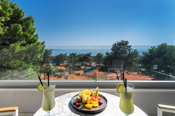 Una mesa con una bandeja de frutas y dos bebidas, con vistas a un paisaje escénico de árboles y un horizonte lejano.