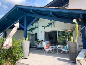 An outdoor patio with a blue roof, a cactus, and a dining area with chairs and a table. - BIARRITZ in summer, villa golf de BASSUSSARRY heated swimming pool (Bassussarry)