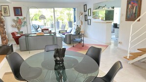Uma sala de estar moderna com uma mesa de jantar de vidro, rodeada por cadeiras pretas, um sofá cinzento e uma poltrona vermelha.