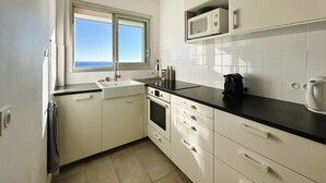 Cocina compacta con ventana, armarios blancos, microondas y cafetera.