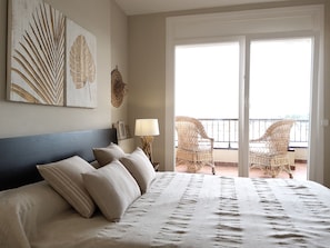 Relax in this serene space with a large bed, wall-mounted artwork, and a balcony with outdoor views.
