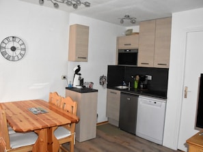 Cozinha compacta com mesa de jantar de madeira, cafeteira e máquina de lavar louça.