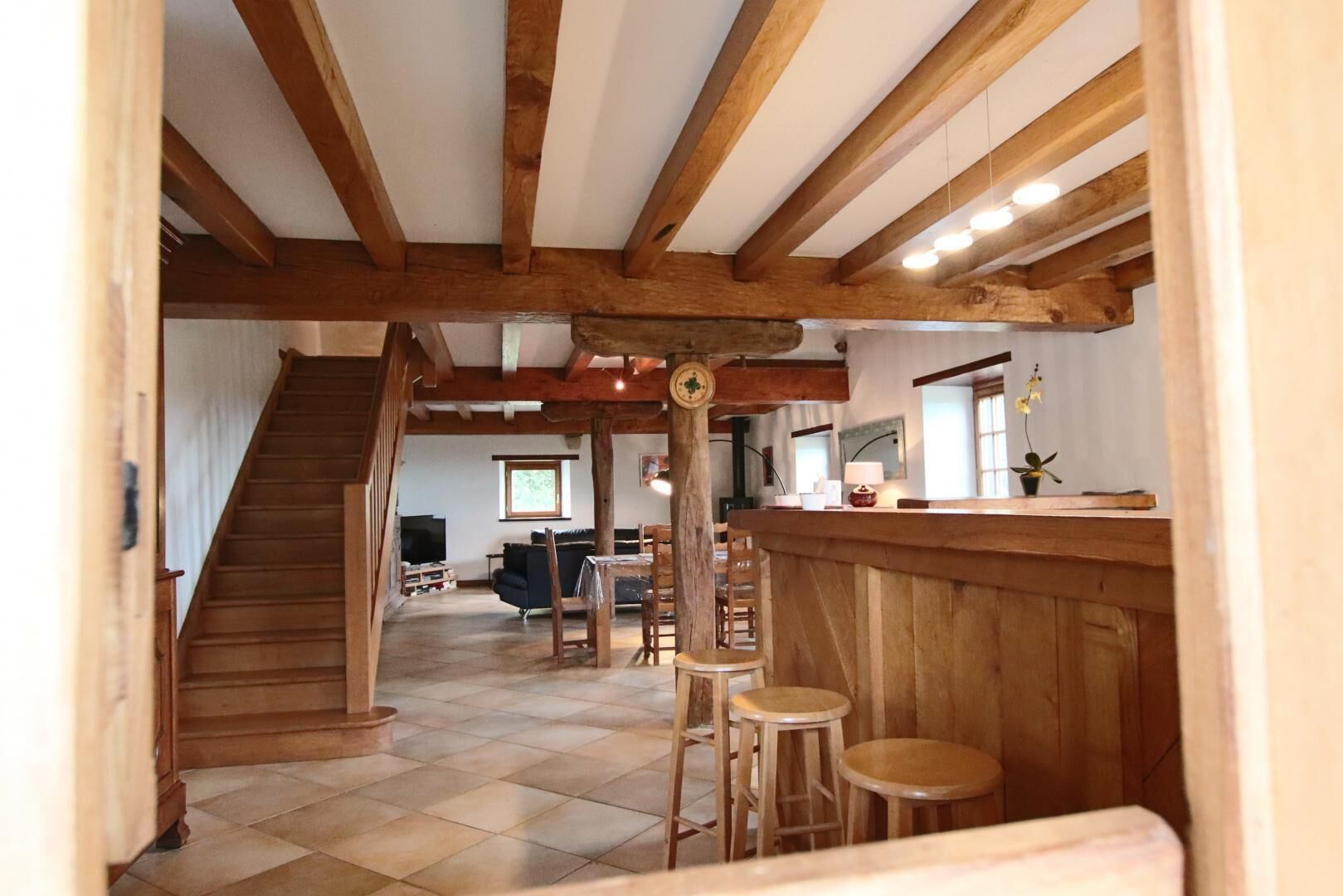 Una habitación amplia con una escalera de madera, un comedor con taburetes y una barra.