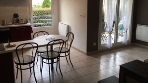 A modern kitchen with a dining area, a window with a red blind, and a view of greenery outside. - Lovely T2 garden apartment with sheltered terrace swimming pool (summer) Fibre  (Albertville)
