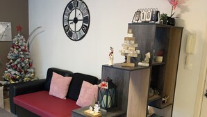 A living room with a red sofa, a wooden coffee table, a clock, a Christmas tree, and a bookshelf with various items. - Lovely T2 garden apartment with sheltered terrace swimming pool (summer) Fibre  (Albertville)
