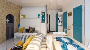 Una habitación de hotel moderna con una cama, un sofá, una mesita y un baño visible a través de una puerta abierta.