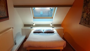 A bedroom with a skylight, a bed with striped bedding, bedside lamps, and a radiator. - Villa Azious, 10 persons, beach side in Wimereux with parking possibility (Wimereux)