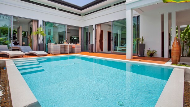 A modern pool area with a clear blue pool, sun loungers, and a covered seating area. - Isawan 2BR Salt Pool Villa in Baannaraya (Rawai)
